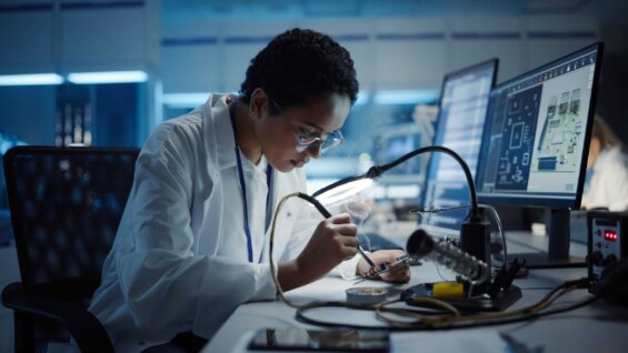 A woman in a lab coat works on a piece of hardware in a laboratory.