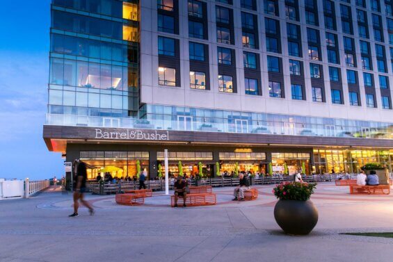 The courtyard in front of a mixed-use building bustling with people at dusk.