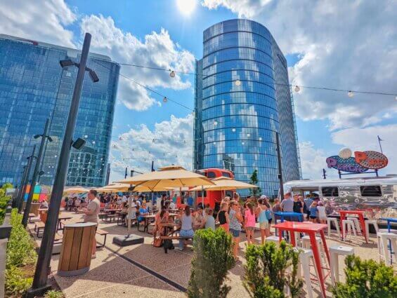 Tall office buildings are visible behind a courtyard teeming with people enjoying lunch on a sunny day at Capital One Center in Tysonsn, Virginia.