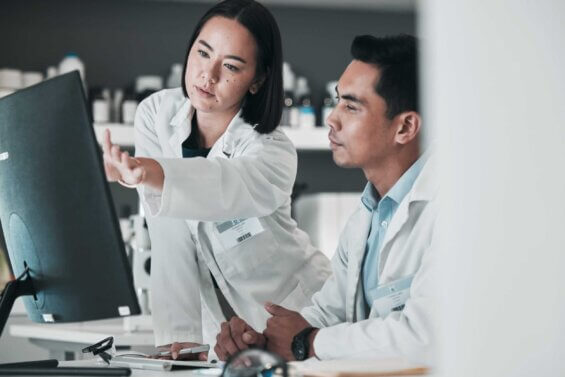 A young female doctor speaks and points at a monitor while her colleague listens.