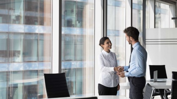 A businesswoman shakes hands with a businessman in a modern office.