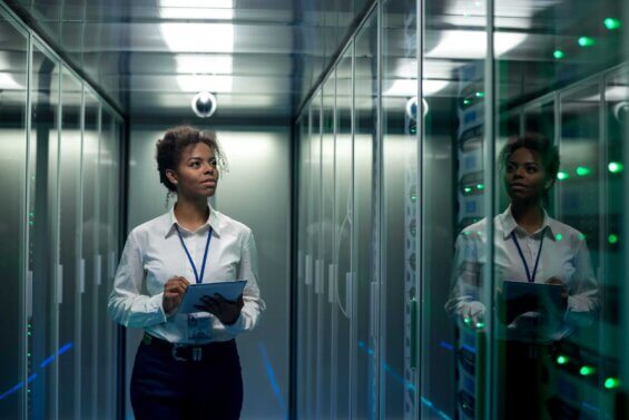 A young woman walks through a data center while holding a tablet.