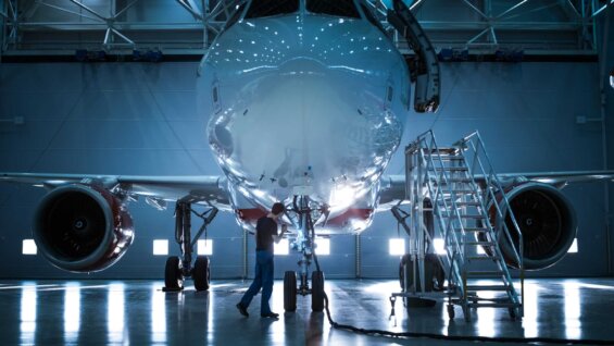 A man walks beneath the body of a brand new airplane in a manufacturing plant.