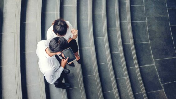 Birds-eye view of two business people consulting a tablet outdoors.