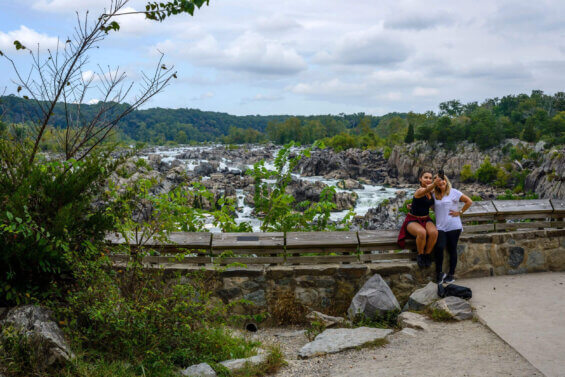 Two women take a selfie in front of a rocky, wooded stream.