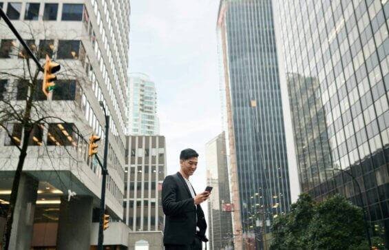 A smiling business man looks down at his phone while in a busy downtown area.