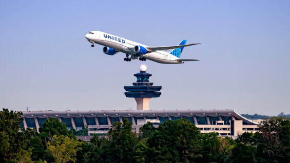 A United Airlines airplane flies over an airport during the day.