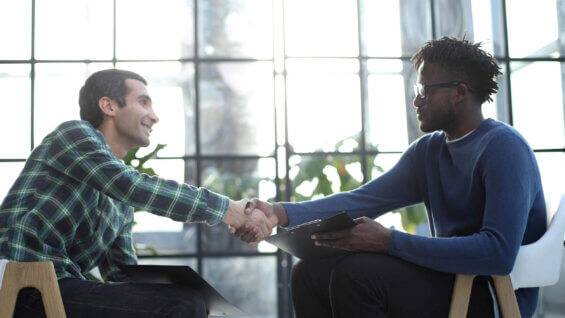 Two men holding clipboards shake hands with each other.